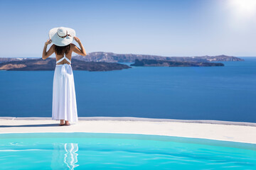 A woman in a white summer dress looks at the beautiful view of the Caldera at Santorini island,...