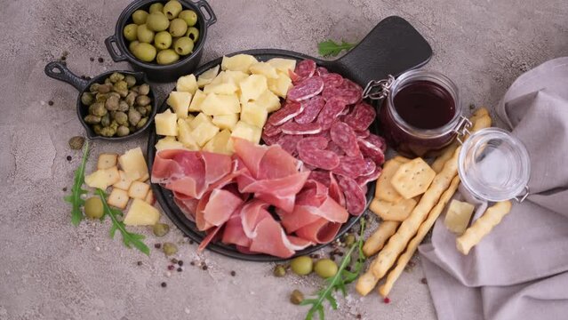 making meat and cheese antipasto plater - woman adding capers and olives to serving board with cheese, prosciutto and fuet sausages