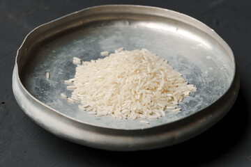 Heap of dry rice in a bowl on black background, lack of food, hunger concept