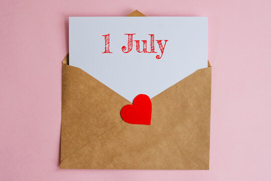 Kraft envelope with a white sheet of paper and a date 1 july, with a red heart. Flat lay on pink background, romance and love concept