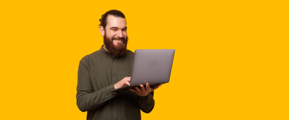 A happy bearded man is typing in his laptop near a free and yellow copy space