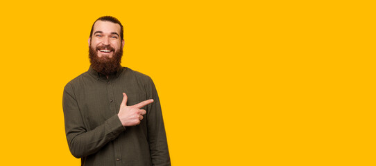 A happy bearded man is looking at the camera and is pointing at a free space near him