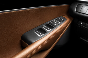 Door handle with power window control buttons of a luxury passenger car. Brown perforated leather...