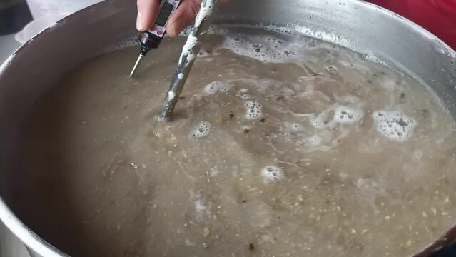 Slow motion footage of the warm brown mash being stirred and its temperature measured. Handheld close up shot of self brewed beer