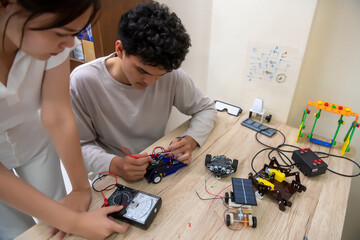 Teenage students build learning with robotic vehicles at desks in STEM engineering science...