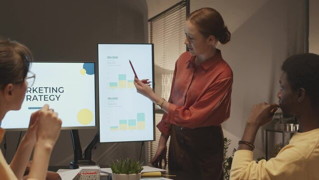 Slowmo of young female marketing specialist making presentation on successful promotion strategy to diverse colleagues sitting at office table and listening