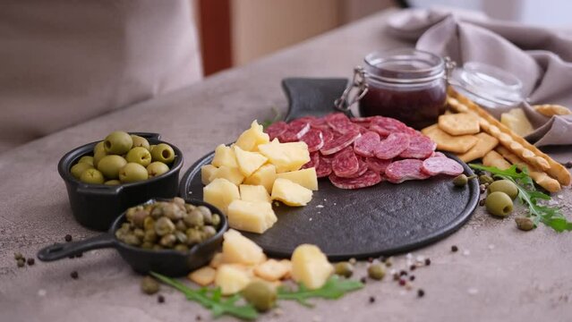 making meat and cheese antipasto plater - woman putting pieces of parmesan hard cheese on stone serving board at domestic kitchen