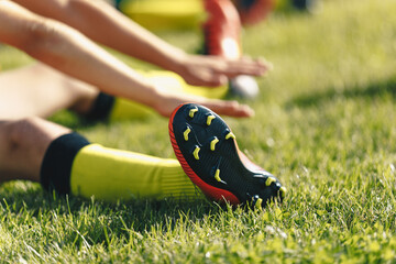 Football Player Stretches Sitting on Grass Pitch. Stretching Session After Workout For Footballers. Player in Soccer Cleats and Socks © matimix