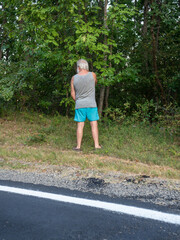 senior caucasian man urinating at roadside, rear view, summertime