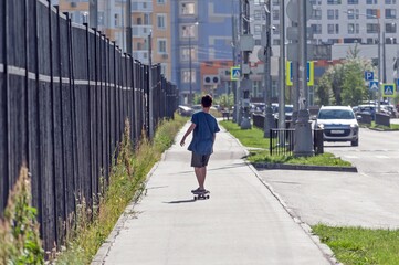 A boy walks along the sidewalk on a skateboard