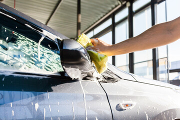 A man washes the mirror on his car with foam at a self-service car wash