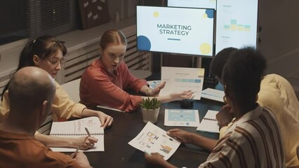 Medium slowmo of hard working and creative multiethnic team of marketing specialists having meeting at office desk at night, discussing marketing strategy for their product - Powered by Adobe