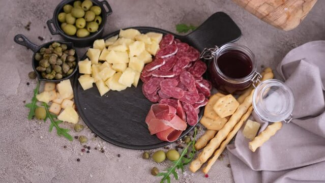 making meat and cheese antipasto plater - woman putting pieces of prosciutto ham on stone serving board at domestic kitchen