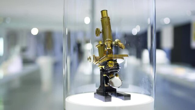 Pan down to an ancient microscope model made from brass, being displayed in an optics museum showcase