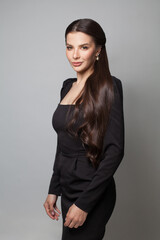 Fashion portrait of beautiful young woman in black dress standing on grey background