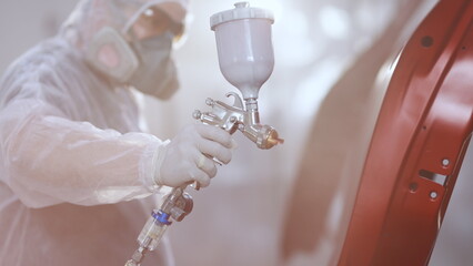 Male technician is air-painting car's door. Industrial spray painting process. Auto painter...