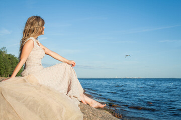 Fototapeta na wymiar Attractive woman in prom dress sitting on a rock by the sea