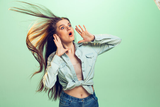 Portrait of young emotive girl in casual clothes posing with shocked expression isolated over green studio background.