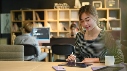 Young female software programmer or coder working in startup company and colleagues sitting in background
