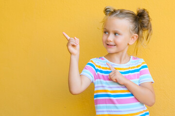 Smiling little kid girl is attracted by attention pointing finger at copy space. The concept of...