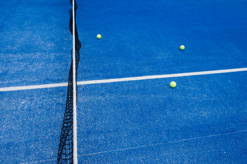 Selective focus. Blue synthetic paddle tennis court and various yellow balls.