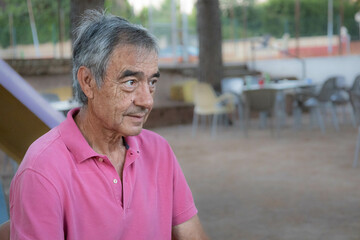 Caucasian man in his 60s with grey hair and pink t- shirt looking something with attention