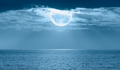 Night sky with moon in the dark clouds and blue sea in the foreground "Elements of this image furnished by NASA"