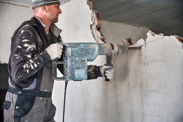 Man builder in workwear drilling wall with electric hammer drill. Male worker using electric drill...