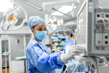 Anesthetist Working In Operating Theatre Wearing Protecive Gear checking monitors while sedating...