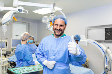 Young male surgeon standing in operating room showing thumbs up, ready to work on a patient. Male medical worker surgical uniform in operation theater.
