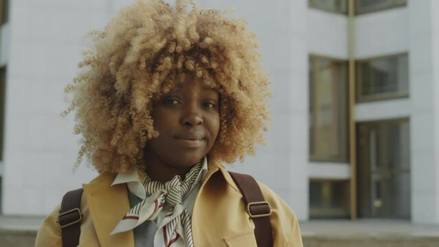 Portrait of young African American woman with backpack standing outdoors on city street and posing for camera