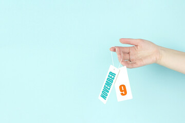 November 9th. Day 9 of month, Calendar date. Hand hold price tag with calendar date on blue...