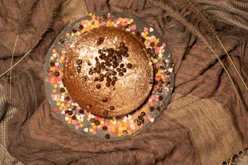 chocolate sponge cake decorated with powdered sugar, cocoa powder, chocolate chips or shavings, with hearts and sugar stars in white and pink on a background of crumpled fabric. with space for writing