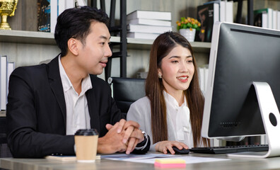 Asian young professional businesswoman secretary sitting smiling working typing with computer while successful businessman entrepreneur in formal suit helping coaching training in company office
