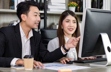 Asian young professional businesswoman secretary sitting smiling working typing with computer while successful businessman entrepreneur in formal suit helping coaching training in company office