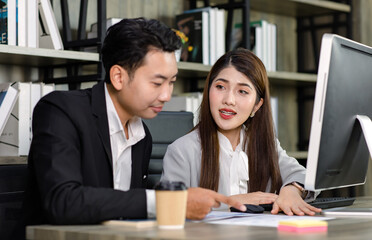 Asian young professional businesswoman secretary sitting smiling working typing with computer while successful businessman entrepreneur in formal suit helping coaching training in company office
