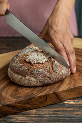 Hands of a woman holding and cutting a rustic sourdough bread with knife - stock photo