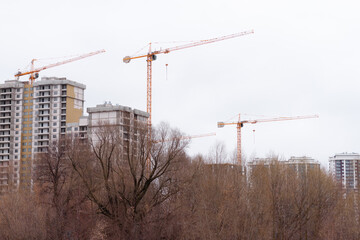Tall residential buildings under construction in the far away. A dirt road is leading to the side of the frame. Several cranes on the background