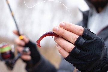A closeup of a rubber red fish bait hooked on the hook and prepared for the fishing. A hand holding...