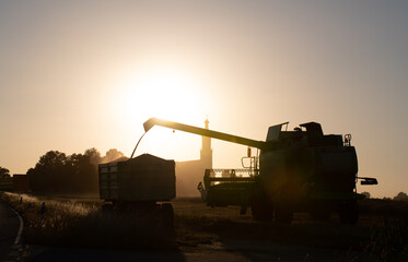 A harvester mowing grain in Bavaria in the evening. In the background a church and the sunset.