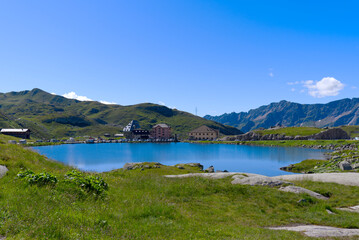 Naklejka na ściany i meble Scenic landscape at hiking trail at Swiss mountain pass St. Gotthard with mountain lake and historic Tremola road on a sunny summer day. Photo taken June 25th, 2022, Gotthard Pass, Switzerland.