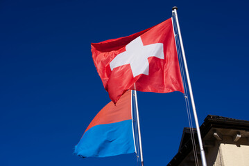 Swiss flag and flag of Canton Ticino waving at famous Swiss mountain pass St. Gotthard on a sunny summer day. Photo taken June 25th, 2022, Gotthard Pass, Switzerland.