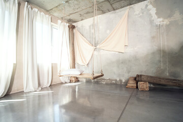 Photo of modern concrete designer interior with wooden swing with pillow. Natural sunlight.