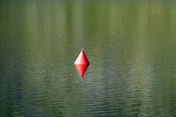 Red buoy at mountain lake with beautiful reflections in water at Gotthard Pass summit on a sunny summer day. Photo taken June 25th, 2022, Gotthard Pass, Switzerland.