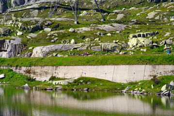 Fototapeta na wymiar Scenic landscape at hiking trail at Swiss mountain pass St. Gotthard with mountain lake and historic Tremola road on a sunny summer day. Photo taken June 25th, 2022, Gotthard Pass, Switzerland.