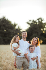 Beautiful young family at sunset in a wheat field. Happy parents with two children, a boy and a girl, in light clothes. Summer.