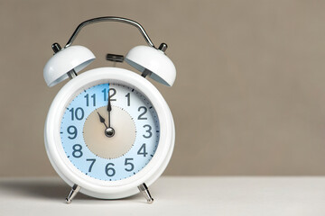 Eleven o'clock on the alarm. A white alarm clock is on a white table. The clock hand points to 11 o'clock. Time to change to summer or winter time. Set an alarm for 11:00 or 23:00. copy space