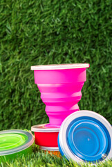 Modern pink collapsible silicone cup on the background of green nature. reusable thermos bottle. Go plastic free. No waste - obrazy, fototapety, plakaty