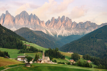 Stunning view of the Funes Valley (Val di Funes) with the Santa Maddalena Church and the mountain range of the Puez Odle Nature Park in the distance during a beautiful sunset. Santa Magdalena, Italy.