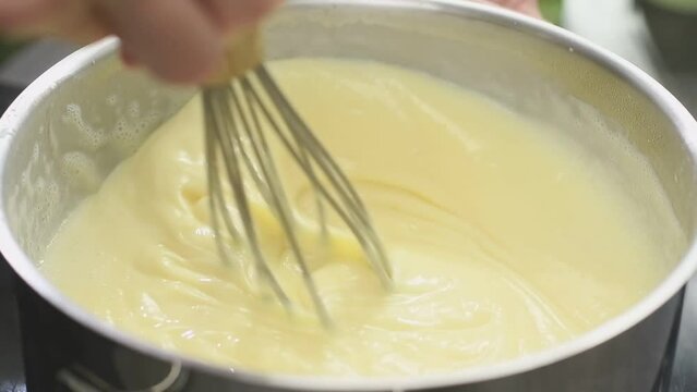 Cooking and stirring of vanilla pudding in a saucepan.